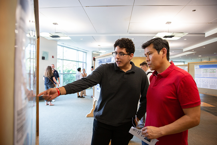 A chemistry student discusses his research with his advisor at a poster exhibition.