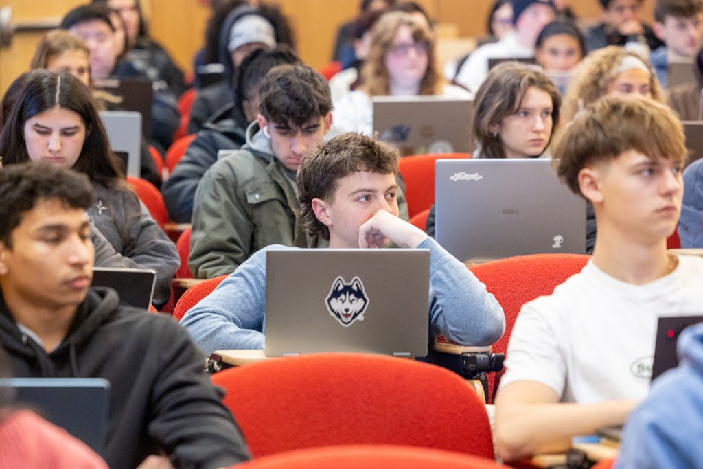 Students with laptops listening to a lecture in a large classroom. 