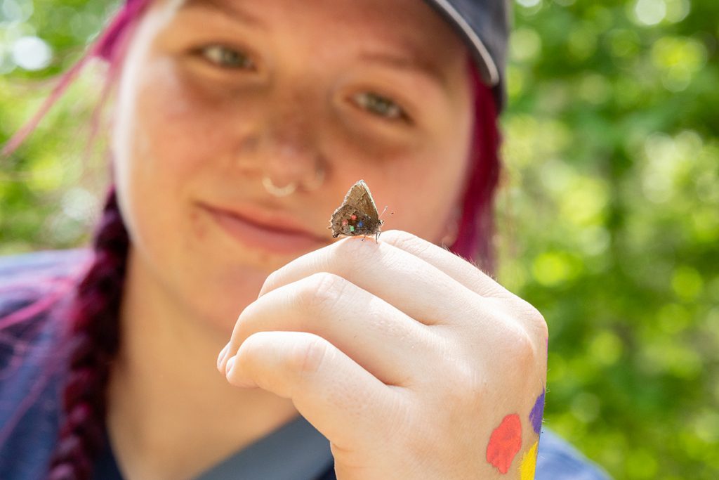 A student holds a butterfly while conducting field research.