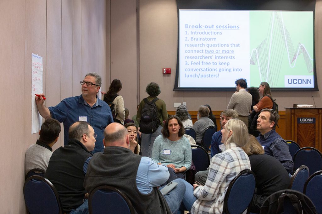 A large group of researchers sit in a circle and discuss a topic during an Institute for the Brain and Cognitive Sciences collaboration event.