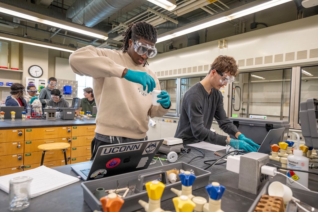 Two students in googles and globes conduct an experiment in a chemistry lab.