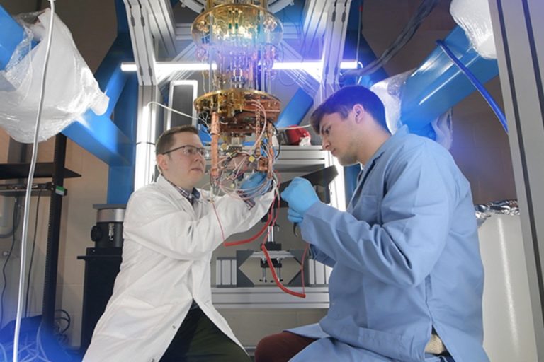 Two physics researchers hold equipment while wearing lab coats.