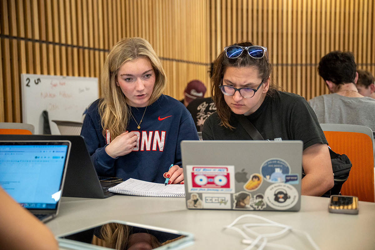 Two students look at a laptop while working on a group project in class. 